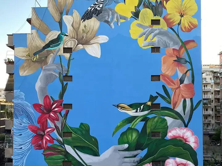 Il murale Sereno di Daniele Geniale: fiori, uccelli e mani su una facciata azzurra di otto piani in via di Santa Maria Goretti a Roma